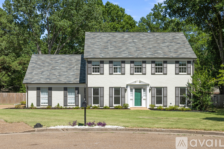 A white house with a green door and windows surrounded by a grassy area.