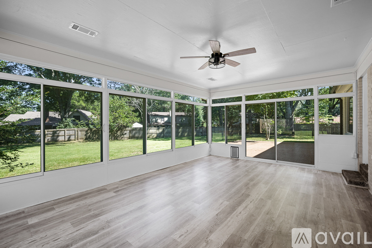 A spacious room with a ceiling fan and large windows overlooking a garden.