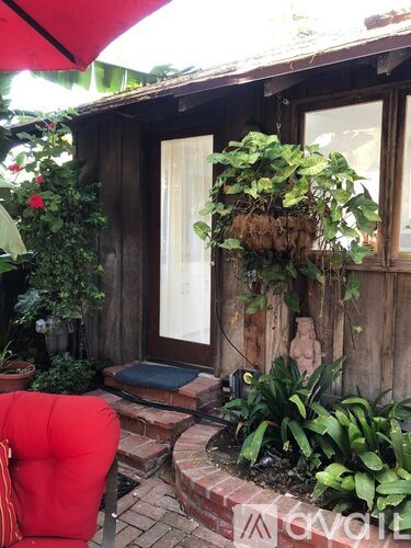 A red chair is in front of a wooden building with a planter hanging from the window.