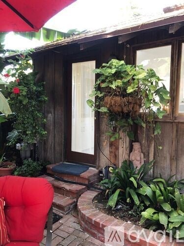 A red chair is in front of a wooden building with a planter hanging from the window.