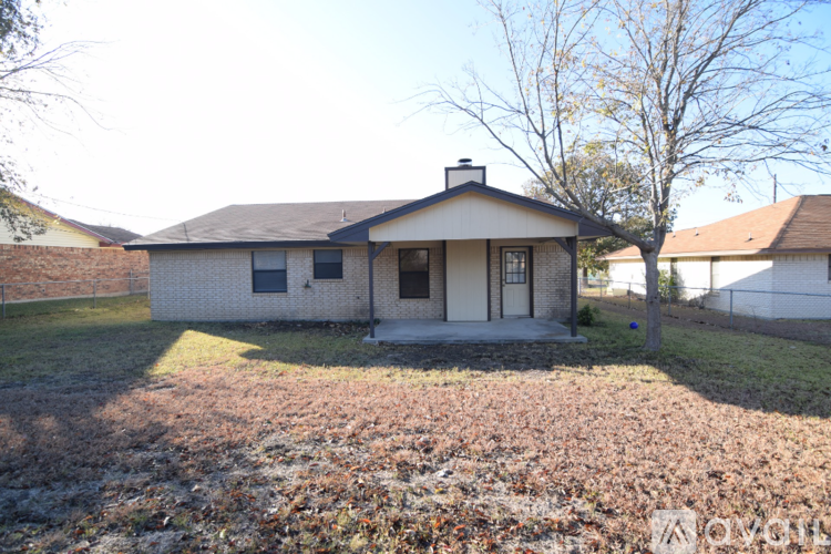 A house with a brick chimney is surrounded by a grassy area with fallen leaves.