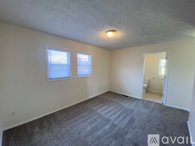 A room with a carpeted floor and two windows.