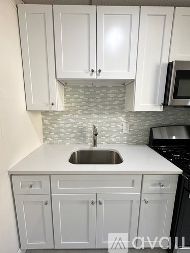 A kitchen with white cabinets and a grey backsplash.