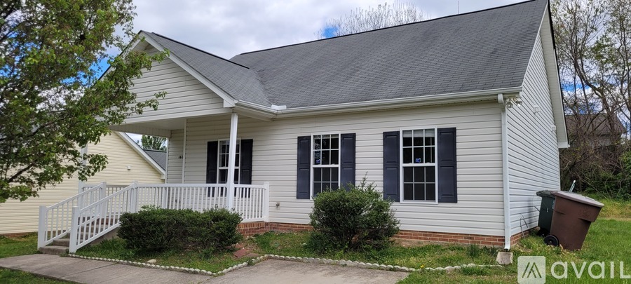 A small house with a porch and a trash can in front.