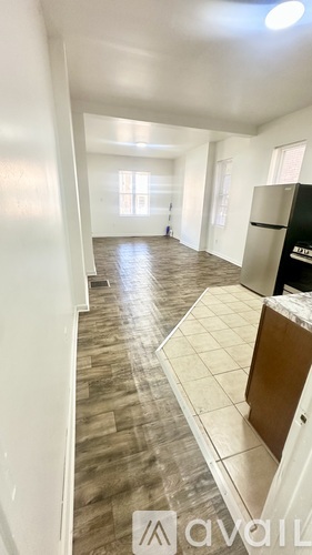 A kitchen area with a black fridge and wooden flooring.