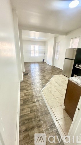 A kitchen area with a black fridge and wooden flooring.