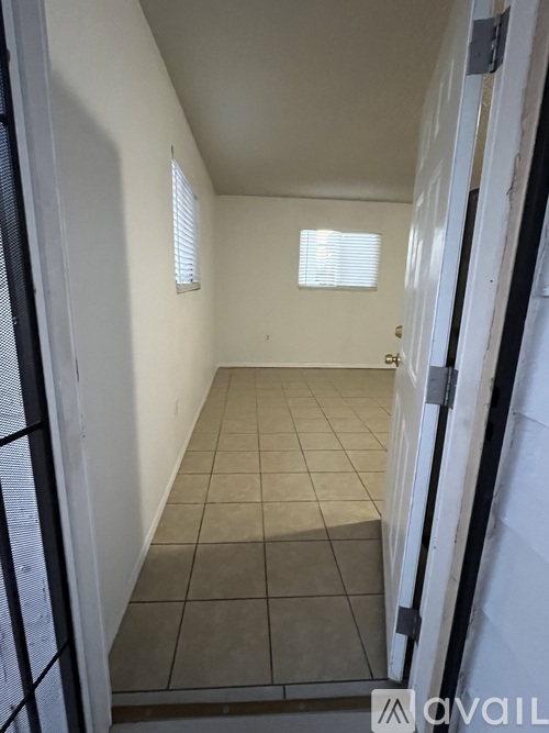A small, empty room with tiled flooring and a window with blinds.