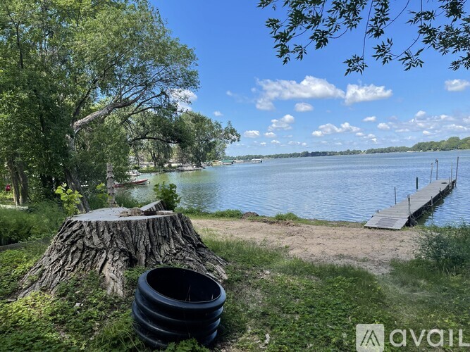 A tree stump sits next to a black barrel on a grassy area by a body of water.