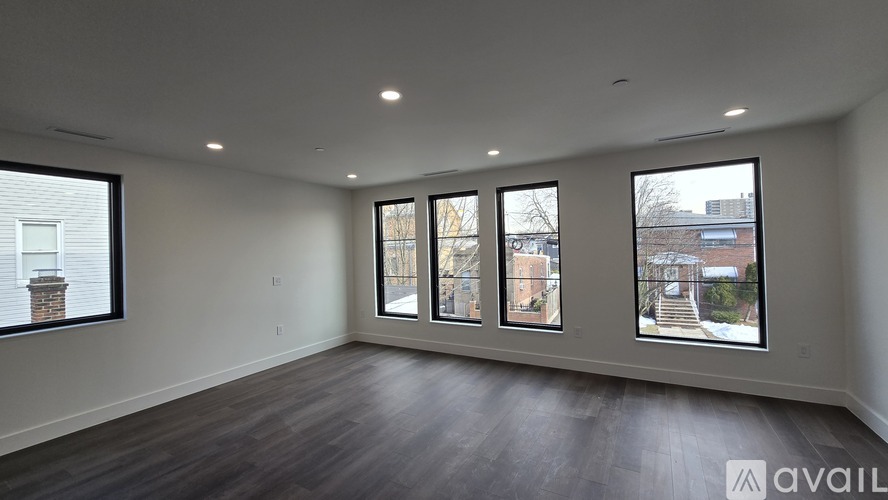 A spacious room with wooden floors and large windows showing an outdoor staircase and buildings.
