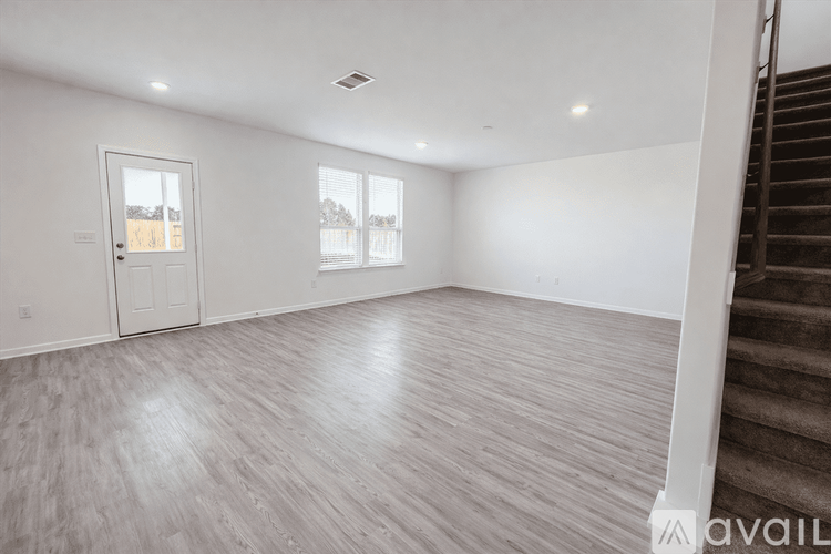 A spacious room with wooden flooring and a staircase on the right side.