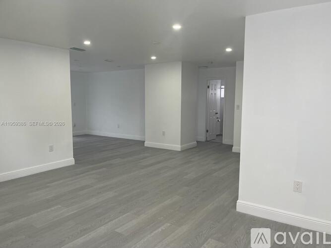 A spacious room with wooden flooring and white walls.