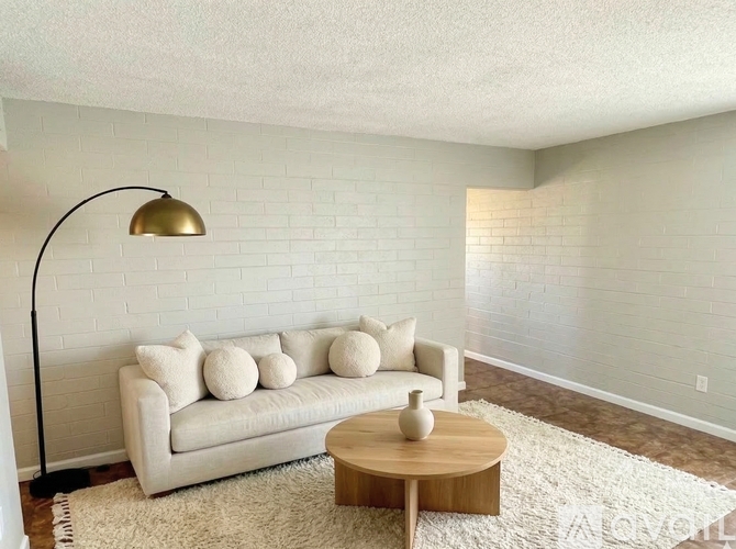 A white couch with a wooden coffee table in front of a white brick wall.
