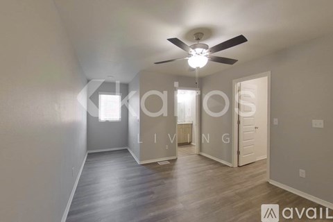 A spacious living room with a ceiling fan and a door leading to another room.
