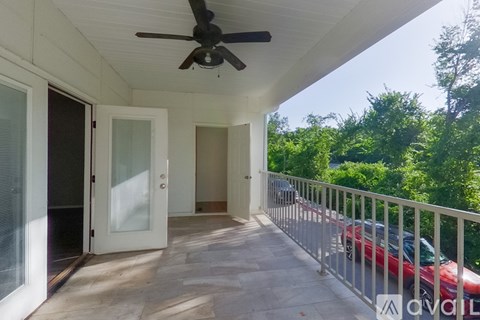 A balcony with a ceiling fan and a red car parked on the street.