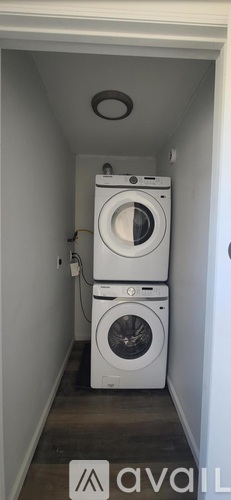 A white washing machine is in a small, white-walled laundry room.
