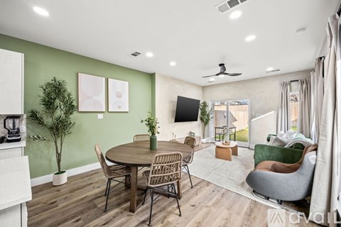 A living room with a round table and chairs, a flat screen TV, and a ceiling fan.