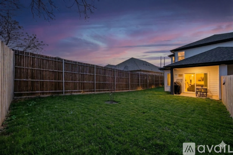 A backyard with a wooden fence and a house with a lit up entrance.