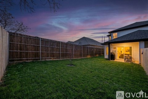 A backyard with a wooden fence and a house with a lit up entrance.