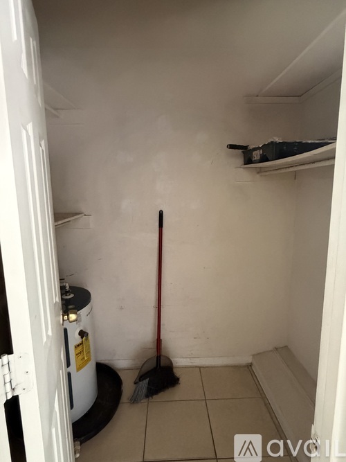 A broom is leaning against a wall in a small, white room.