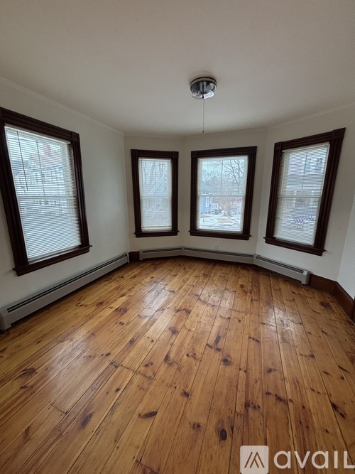 A room with wooden flooring and three windows.