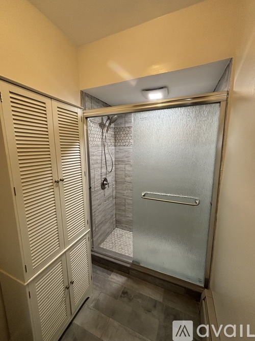 A bathroom with a glass door shower and a wooden cabinet.