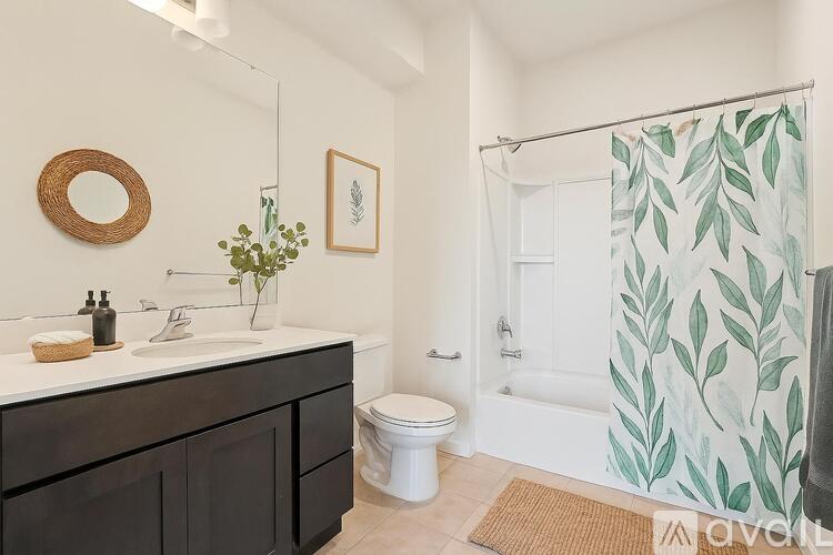 A bathroom with a sink, toilet, and a shower with a leaf patterned shower curtain.