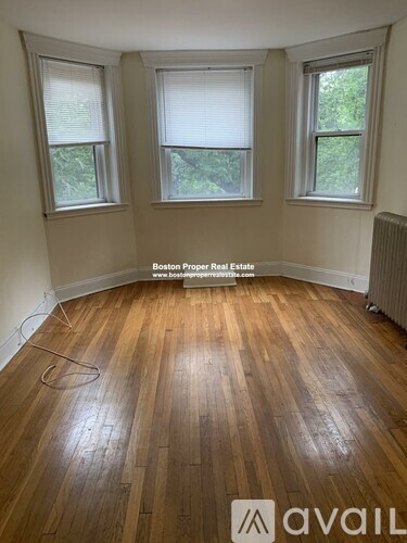 A room with wooden flooring and three windows.