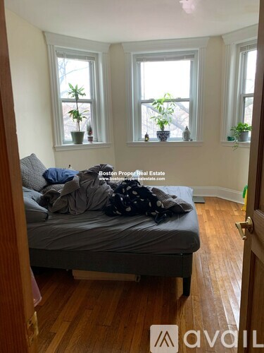 A bedroom with a bed, two windows, and a wooden floor.