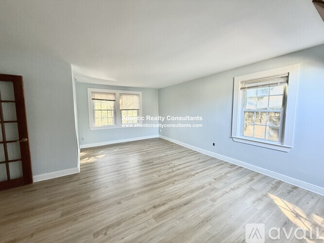 A room with wooden flooring and two windows, one of which is open.