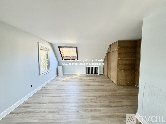 A room with wooden floors and white walls, with a window and a wooden staircase.