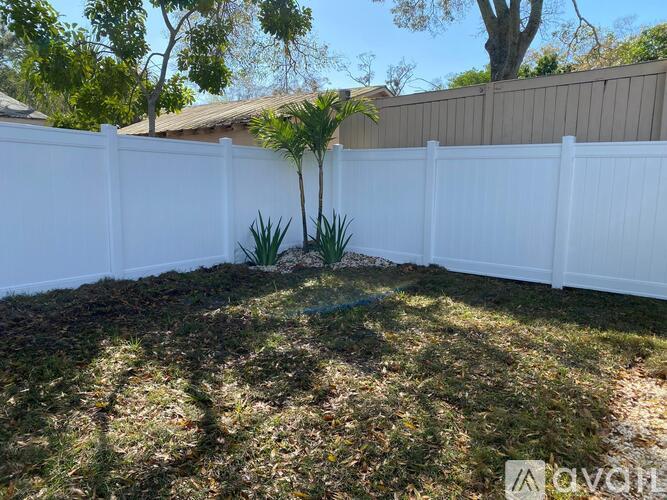 A white fence encloses a yard with a small tree and grass.
