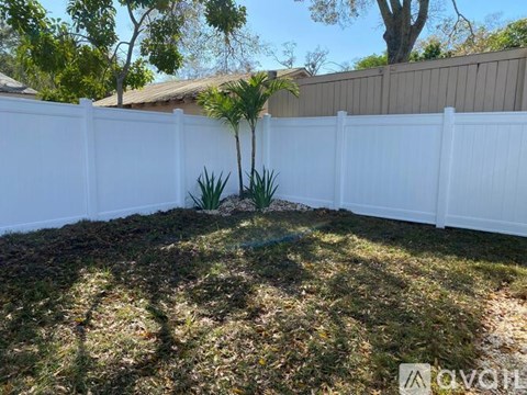 A white fence encloses a yard with a small tree and grass.