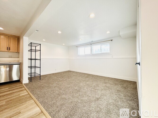 A spacious room with a carpeted floor, a window, and a white wall.