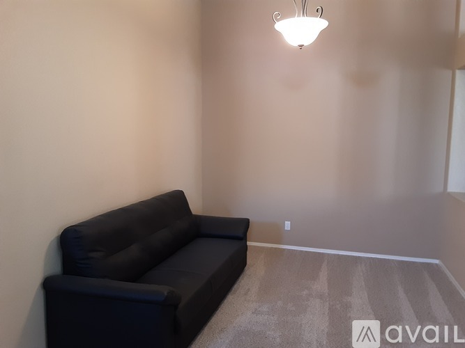 A black couch sits in a room with a light on the wall.