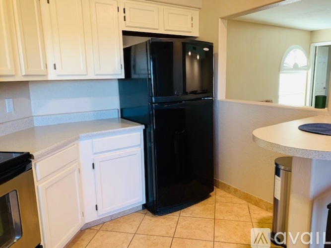 A black refrigerator in a kitchen with white cabinets.