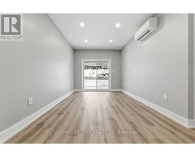 A spacious room with wooden flooring and a white wall with a realtor logo.
