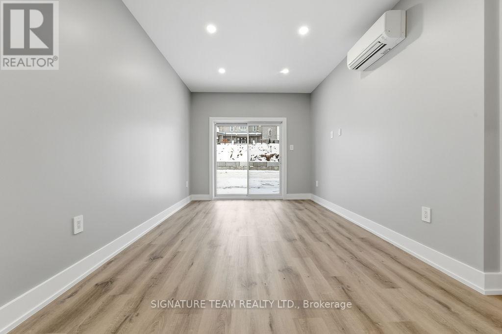 A spacious room with wooden flooring and a white wall with a realtor logo.