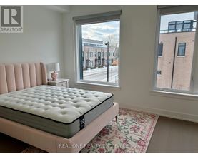 A bedroom with a large bed and a view of a street outside the window.
