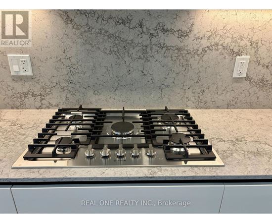 A stove top with a silver finish is in a kitchen with a marble counter top.