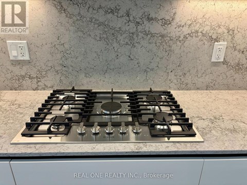 A stove top with a silver finish is in a kitchen with a marble counter top.