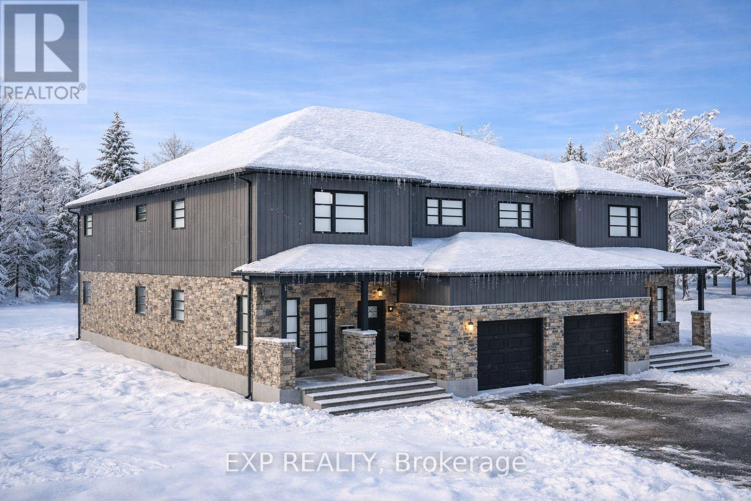 A large house with a stone wall and a black roof covered in snow.