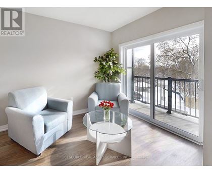 A living room with a grey couch, a white chair, and a glass table with a vase of flowers on it.