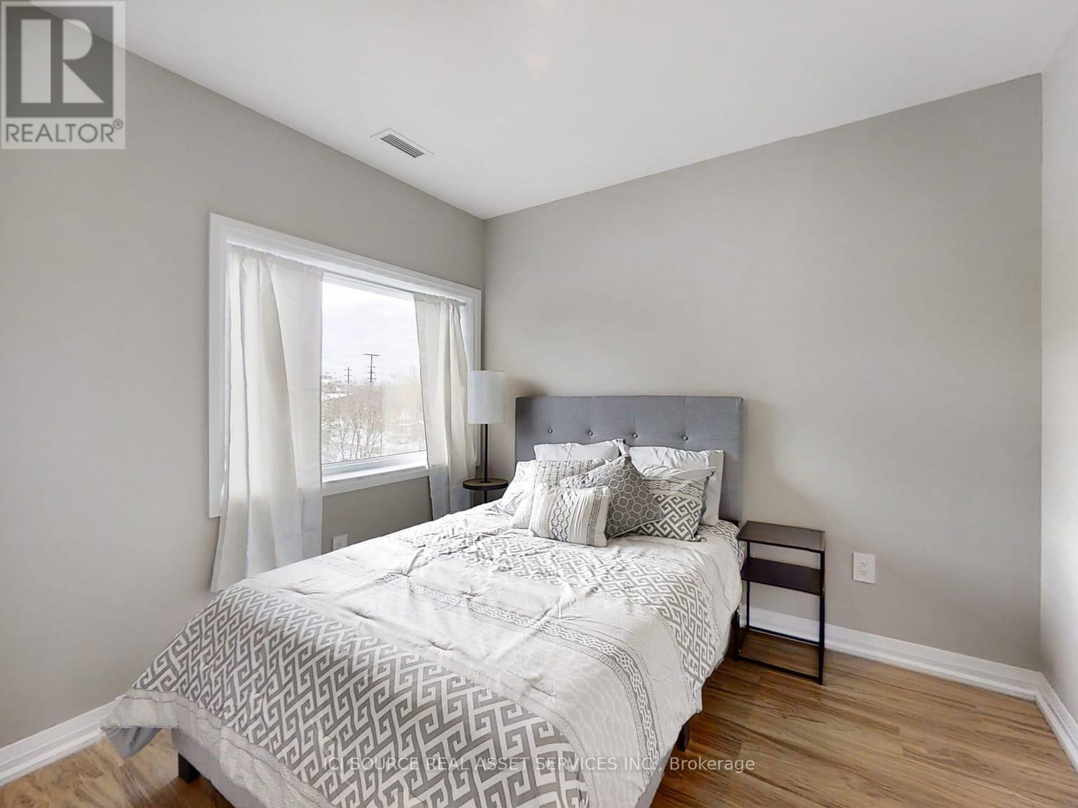 A bedroom with a large bed and a window with white curtains.