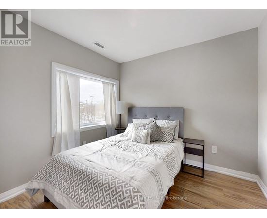 A bedroom with a large bed and a window with white curtains.