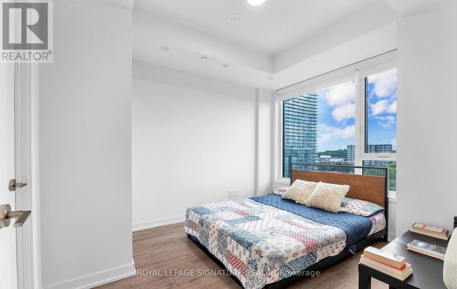 A bedroom with a bed, nightstand, and window overlooking a cityscape.