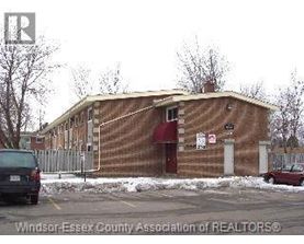 A building with a red awning is in front of a fence and a car.