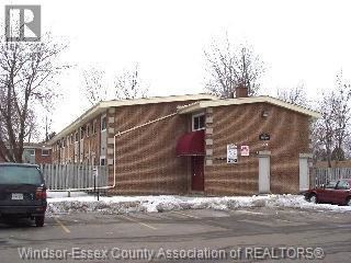 A building with a red awning is in front of a fence and a car.