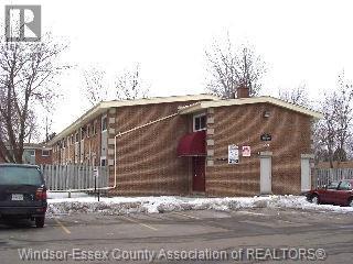 A building with a red awning is in front of a fence and a car.
