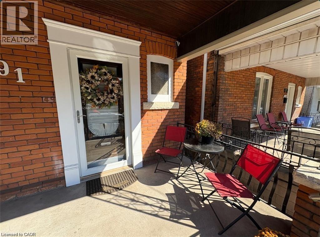A patio with a table and chairs is in front of a brick building with a realtor sign.