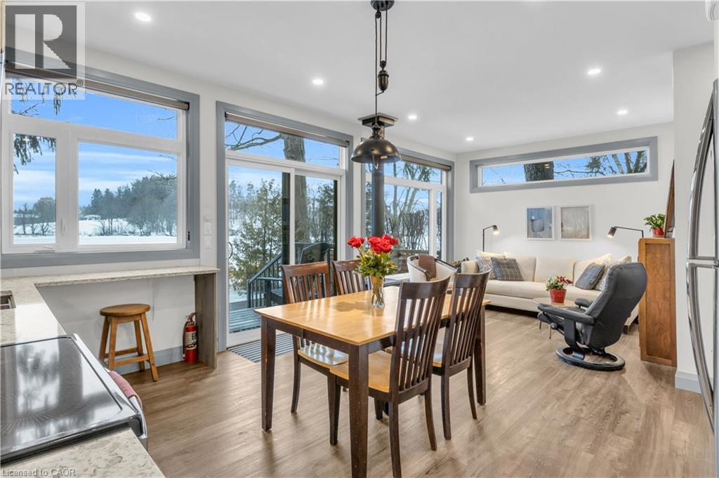 A dining room with a wooden table and chairs, a couch, and a view of the outdoors through large windows.